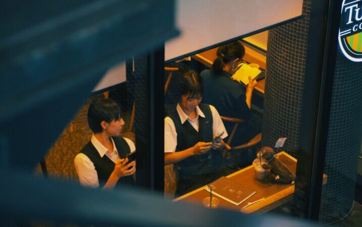 スマートフォンを操作する高校生たち。日常の中で言葉の変化が生まれる現代のコミュニケーションの象徴